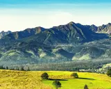 Widok na Tatry po angielsku: zielone wzgórza, lasy i skaliste szczyty. W oddali widać małą wioskę.