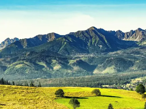 Widok na Tatry po angielsku: zielone wzgórza, lasy i skaliste szczyty. W oddali widać małą wioskę.